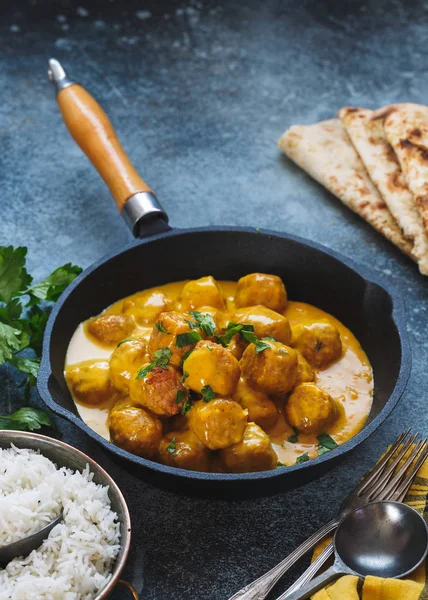 Spicy curry dish with meatballs served with pilau rice and naan bread, selective focus