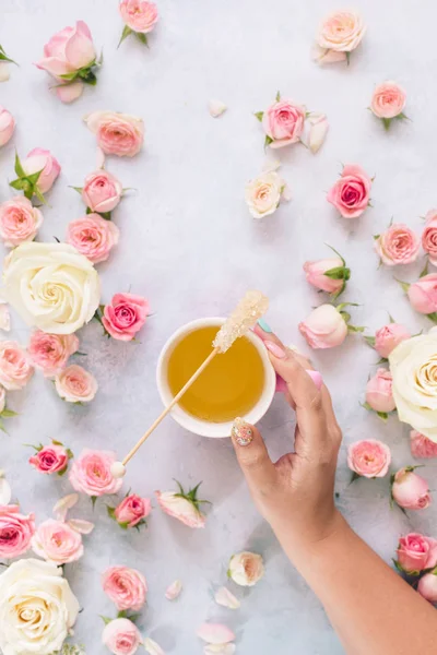 Flat lay with woman's hand holding cup of tea surrounded by various roses and petals, textured background. Morning,  drink,  break