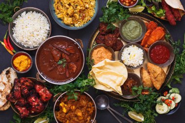 Rogan Josh, tavuk tikka masala, biryani, tandır tavuk, kebap ve samosa, pakoras, soğan bajis, poppadoms, naan ve dips, üst görünümü ile karışık hint tabağı içeren çeşitli Hint yemekleri