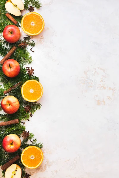 Christmas fresh  fruit background border with orange half, spices, apple whole and half and natural fir tree over golden white rustic surface, top view