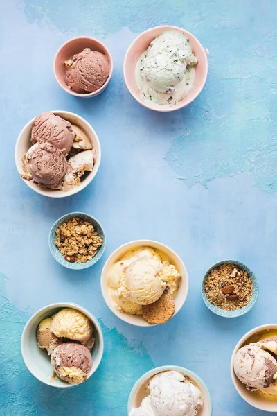 Different flavors of ice cream in small bowls on rustic blue background. Top view, blank space