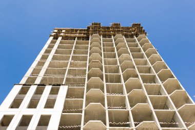  Mavi gökyüzüne karşı modern bir monolitik konut binasının cephesi. Binanın tamamlanmamış inşaatı.