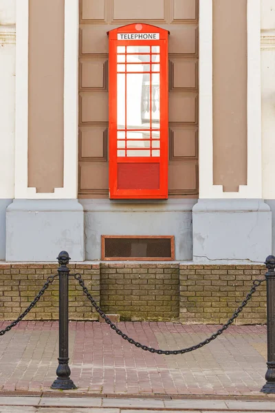 Red telephone box icon London, suspended on the wall of the house. Traditional red British telephone box