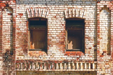 Pencereleri tahtayla kapatılmış eski tuğla duvar. Eski depo, eski şehir mimarisi. Pencere açıklıkları ile yıkılan ve yıpranmış tuğlalardan oluşan tuğlalar.