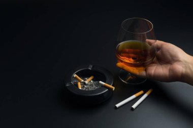 bir bardak konyak, Sigara ve siyah seramik kül tablası ile sigara izmaritleri, küllerinden tam siyah masaya tutan el
