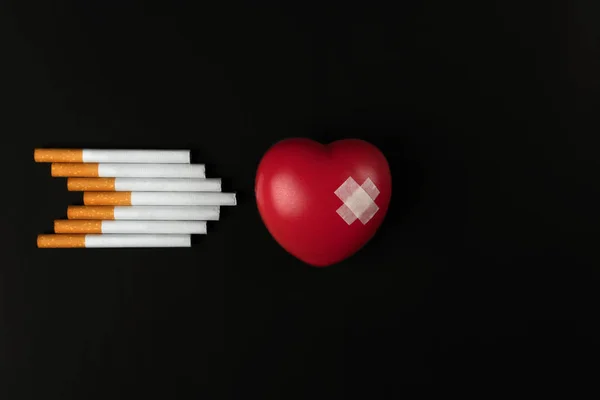 抽烟杀死概念 红色心脏标志用黏贴石膏和一组香烟在箭头形状在黑暗的背景上 — 图库照片