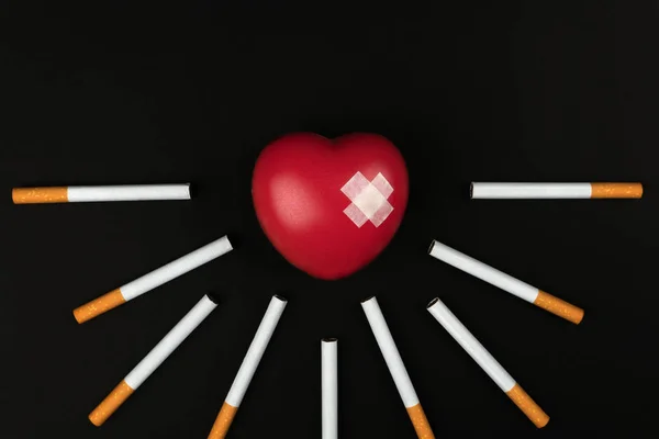 吸烟杀死概念 红色心脏标志在香烟之间在黑暗的背景上的粘附石膏 — 图库照片