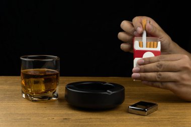 bir sigara paketi alarak ver. bourbon viski, bir siyah seramik küllük ve bir krom ahşap masa üzerinde hafif bir bardak.