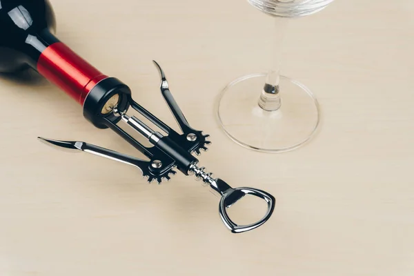 a red wine bottle with a metal corkscrew and an empty wine glass on the wooden table