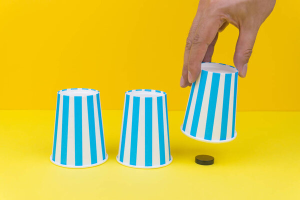 Hand lifting up a blue party paper cup and found a black wooden round object, yellow background