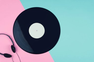 üstten görünüm uzun bir oyun vinil kaydı ya da Lp ile pembe ve mavi arka plan üzerinde siyah bir kulak içi kulaklık