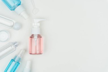 Beyaz arka plan üzerinde pembe, mavi ve net sıvı kapları krem kavanoz ve makyaj spatula ile üstten görünüm