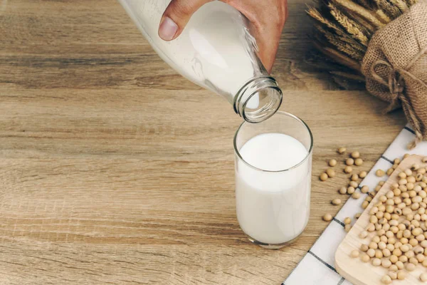 Versando Mano Latte Soia Dalla Bottiglia Bicchiere Mucchio Semi Soia — Foto Stock