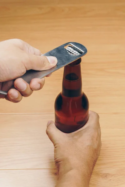 close up hand using a stainless steel bottle opener or bar blade to open a bottle of beer