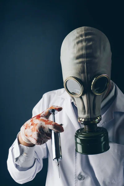 恐怖的医学实验概念 一个可怕的医生在防毒面具戴着血淋淋的手套与一个大的不锈钢注射器在黑暗的背景下 — 图库照片
