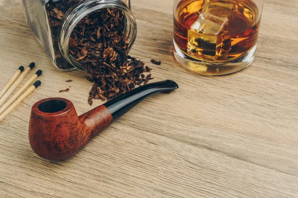 a smoking pipe with tobacco jar, matches and a glass of whisky on wooden table