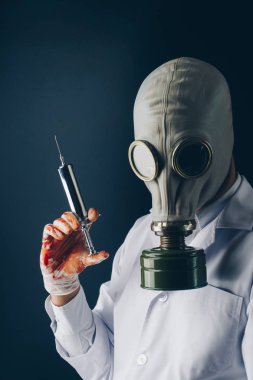 Ürpertici tıbbi deneme kavramı, gaz maskesi koyu arka plan üzerinde büyük paslanmaz çelik şırınga kanlı eldivenler korkunç bir doktor