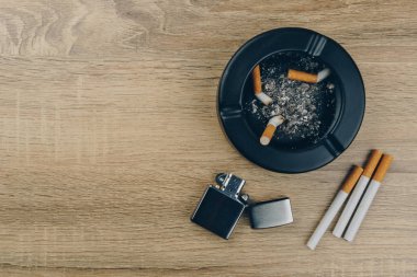 Sigara, metalik çakmak ve siyah seramik küllük küllerinden tam ahşap masa üzerinde sigara izmaritleri ile