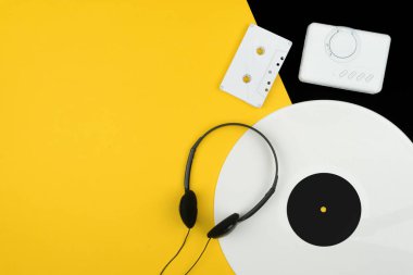 üstten görünüm beyaz uzun bir vinil kaydı, siyah kulaklık ve bir beyaz ses Kaset beyaz bir taşınabilir kaset çalar ile sarı ve siyah arka plan üzerinde oynamak