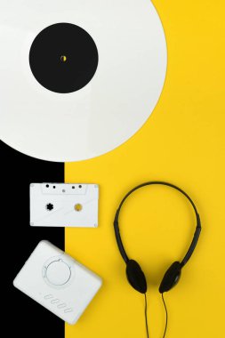 üstten görünüm beyaz uzun bir vinil kaydı, siyah kulaklık ve bir beyaz ses Kaset beyaz bir taşınabilir kaset çalar ile sarı ve siyah arka plan üzerinde oynamak