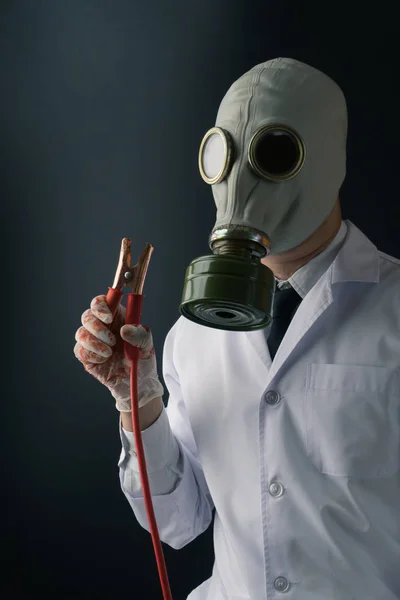 悪と不気味な医学実験概念 暗い背景にバッテリー ブースター ジャンパー ケーブルと血の手袋を着用ガスマスクで怖い医師 — ストック写真