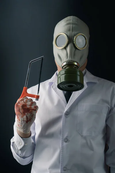 邪恶和恐怖的医学实验概念 一个可怕的医生在防毒面具戴着血淋淋的手套与一只手锯在黑暗的背景 — 图库照片