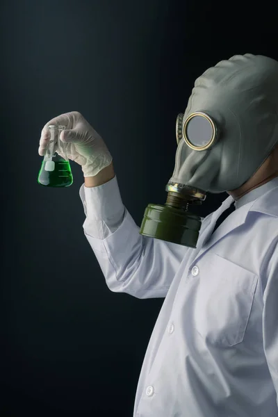邪恶和恐怖的科学实验概念 一个可怕的科学家在防毒面具持有绿色有毒化学物质瓶在黑暗的背景下 — 图库照片