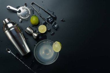 Margarita cocktail glass and bar equipments, stainless steel cocktail shaker and jigger, bar spoon with strainer, the lemons and ice tongs with ice cubes on the table clipart