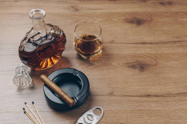 Puro üzerinde siyah seramik kül tablası, bir bardak viski sürahi, bir paslanmaz çelik puro kesici ve ahşap masa maçlarını bourbon viski
