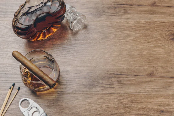 古巴雪茄在一杯波旁威士忌 一个威士忌滗水器与不锈钢雪茄刀和火柴在木桌上 — 图库照片