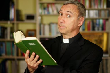 İyi görünümlü bir ciddi Katolik rahip İncil, onun kütüphaneye içe okuma okuyor. Bize desapprovation ile bakar.                               