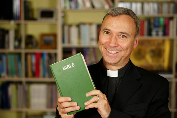 Красивый католический священник изучает Библию в своей библиотеке. Он смотрит на нас с спокойствием и оптимизмом.
.