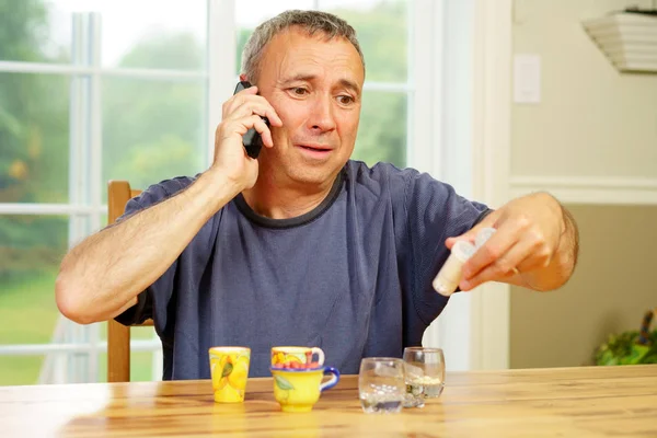 Caucasian man, alone, sit at a table, day, worrying about the pills he is supposed to take.