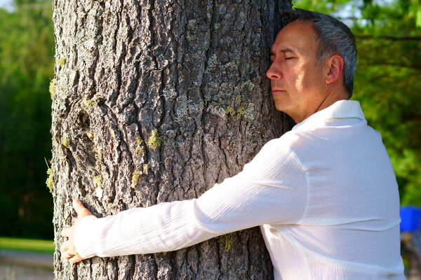 A caucasian man, 50's, is embracing a big tree peacefully to share energy.