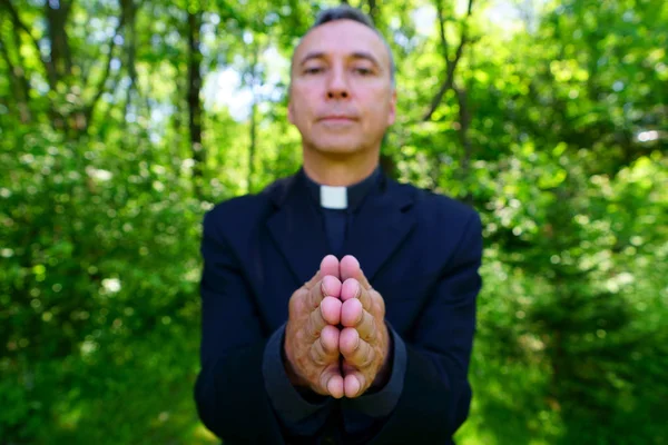 一位漂亮的天主教牧师正与我们一起高兴地祈祷 他自信地看着我们 平静地张开双臂 专注于双手 — 图库照片
