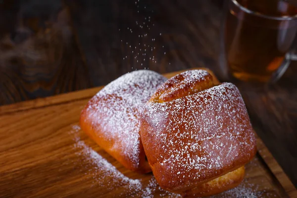 İki lezzetli çörekler krema şeker ile silkeledi. Siyah çay fincan. Ahşap masa üzerinde lezzetli breakfast.