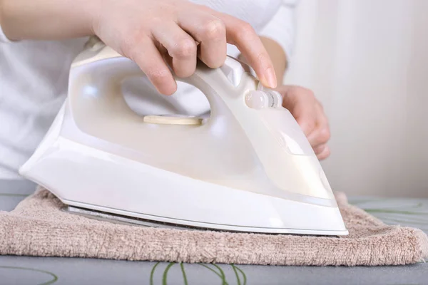 De cerca la mano de la mujer planchando la ropa en la mesa. Mujer joven con planchado visto desde arriba durante las tareas domésticas. Hierro blanco sobre mesa beige . — Foto de Stock