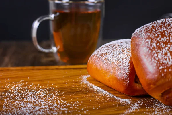 Zwei mit Puderzucker bestäubte Brötchen und eine Tasse schwarzen Tee auf dem Hintergrund. Ansicht von oben — Stockfoto