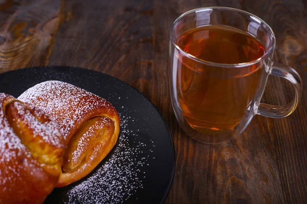 Zwei mit Puderzucker bestäubte Brötchen und eine Tasse schwarzen Tee auf dem hölzernen Hintergrund. Ansicht von oben — Stockfoto