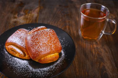 İki çörekler buzlanma şekeri ve ahşap arka planda bir fincan siyah çay ile tozunu. Üst görünüm