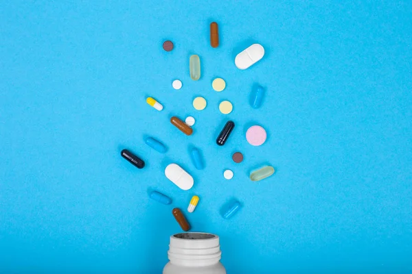 Montón de pastillas y frasco sobre fondo azul, vista superior. Puesta plana — Foto de Stock