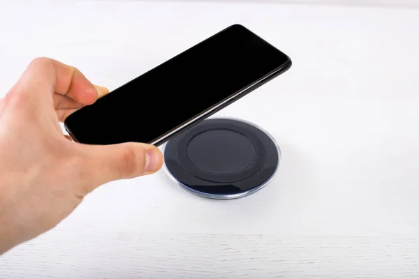 Рука положить мобильный телефон на беспроводное зарядное устройство, современное оборудование на белом фоне — стоковое фото