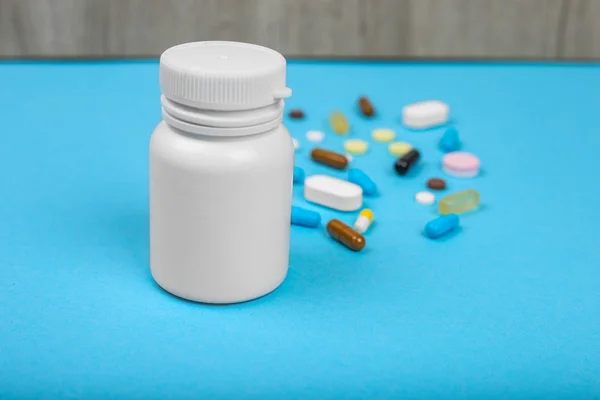 Surtido de píldoras de medicamentos farmacéuticos, tabletas y cápsulas y frasco sobre fondo azul . — Foto de Stock