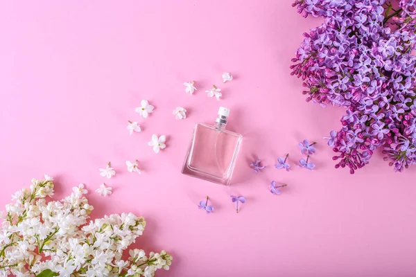 Profumeria e profumo floreale concetto. Bottiglia di profumo al centro con fiori lilla su fondo rosa. Posata creativa alla moda con spazio per il testo . — Foto Stock