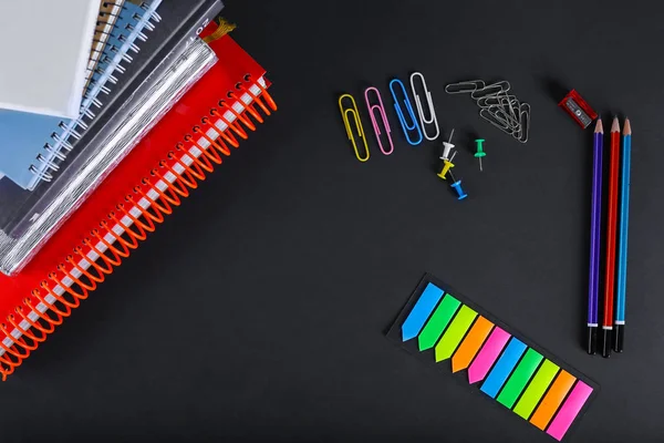Office notepads, paper clips and pencils on a black background. Top view of office things
