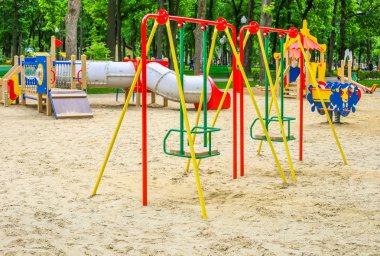 Yeşil ağaçlarla çevrili halka açık parkta renkli çocuk oyun alanı etkinlikleri. Çocuklar modern oyun alanında koşar, kaydır, sallar. Kentsel mahalle çocukluk kavramı.