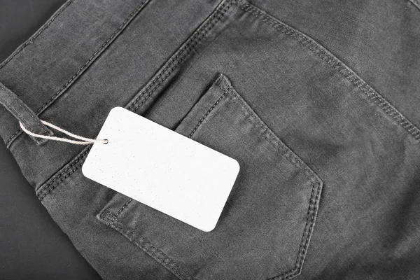 Label price tag mockup on black jeans on black background — Stock Photo, Image