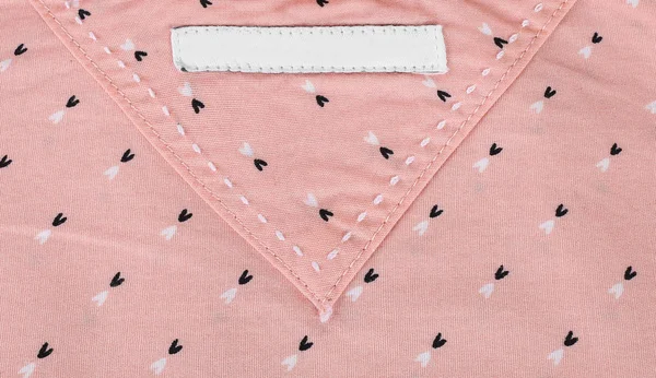 粉红色纺织品背景上空白衣服标签的特写。空白衣服标签模型 — 图库照片