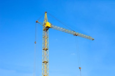 İnşaat Vinç kule mavi gökyüzü arka plan üzerinde. Vinç ve çalışma ilerleme bina. Sarı kaldırma musluk. Metin için boş yer. İnşaat kavramı. Site. Bir vinç ile yeni binalar. Kule vinç