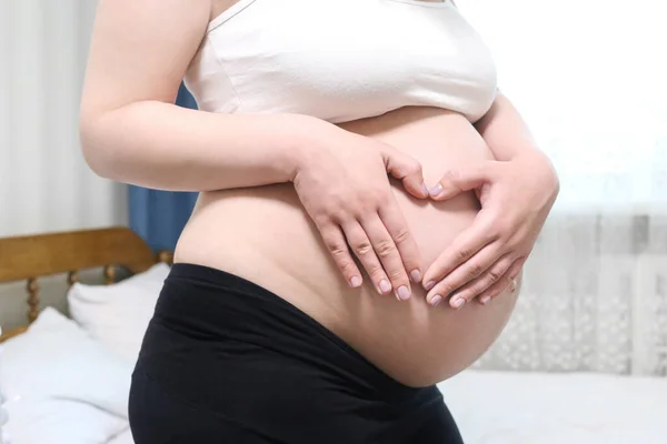 Close-up of a pregnant belly with a heart in the form of hands. Waiting baby. Pregnancy, expectation of child. Future parens. Hands in the form of heart.